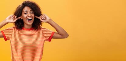 Do not care what saying cannot hear you. Carefree indifferent good-looking african american woman with curly hairstyle closing ears with index finger singing lalala during argument behaving childish photo