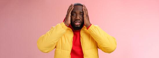 Shocked upset african-american bearded guy feel regret stunned hear terrible news hold hands head widen eyes stupor standing speechless troubled, look perplexed terribly sad, pink background photo