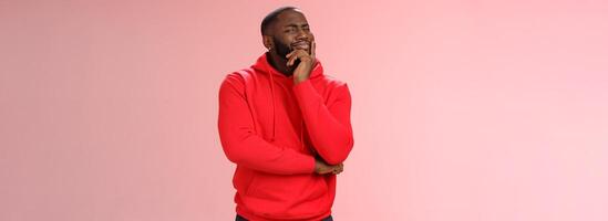 Doubtful sceptical young african-american hesitant bearded guy frowning sarcastic unsure touching chin thoughtful having bad feeling about idea, look disbelief camera, standing pink background photo