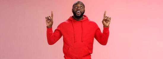 Fascinated attractive black bearded boyfriend gazing shooting star raise head impressed smiling amused pointing up curiously looking upwards, standing pink background enjoy stargazing photo