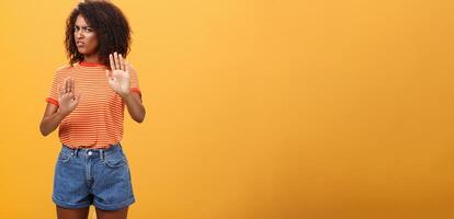 No I refuse. Intense suspicious and displeased smart african-american female rejecting bad offer pulling raised palms turning away with aversion and dissatisfied look against orange background photo