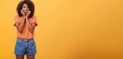 Woman feeling empathy for boyfriend got in trouble standing nervous over orange background biting fingernails frowning and panicking being scared and shocked over orange background photo