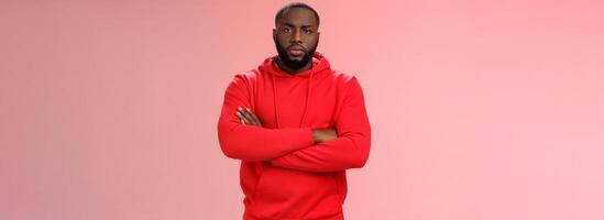 Serious-looking strong black guy security worker cross hands chest confident bossy pose frowning making solid scary look wearing red hooide posing red background, employer controling work photo