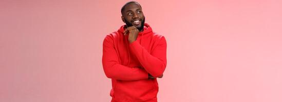 Inetersted successful young black sportsman considering take opportunity look curious upper left corner thinking touch chin thoughtful, make decision choosing what pick, pink background photo