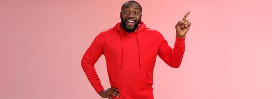 Enthusiastic happy good-looking young black guy beard pointing upper left corner smiling approval like curious about interesting item sale ask question excited impressed, standing pink background photo