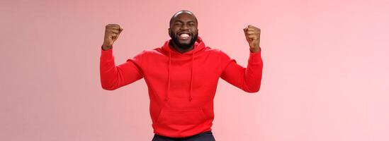 Happy thankful young african american bearded man thank god for son close eyes joyfully smiling clench fists celebrating triumphing dream come true accomplish goal, cheering victory photo