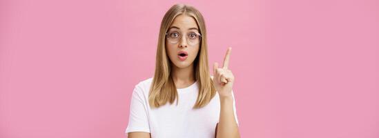 uno más cosa necesitar dicho. inteligente y inteligente hembra un estudiante en lentes y blanco camiseta abierto boca y plegable labios levantamiento índice dedo en eureka gesto agregando sugerencia, teniendo idea foto