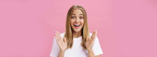 Woman learning awesome great news clasping hands in joy and excitement rejoicing feeling hapyp for friend smiling broadly and looking cheerful at camera with amused expression over pink background photo