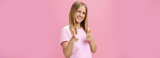 mujer expresando positivo actitud hacia cámara señalando con dedos y parpadeo alegremente sonriente siendo elevado, en pie en bueno estado animico con optimista gestos en contra rosado antecedentes foto