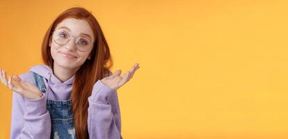 Nothing much. Attractive silly unsure carefree redhead unbothered cute female wearing geek glasses smirking uncertain shrugging hands spread sidways clueless what do future, orange background photo