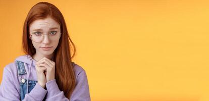 Silly guilty young shy redhead girlfriend asking forgiveness supplicating lower head look from under forehead frowning begging apology favour standing insecure sad pleading help, orange background photo