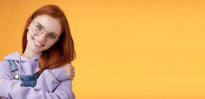 Passion, tenderness, wellbeing concept. Girl accept own self smiling charming grin tilt head hugging herself embracing body feel happiness delighted relaxing, flirty gaze camera orange background photo