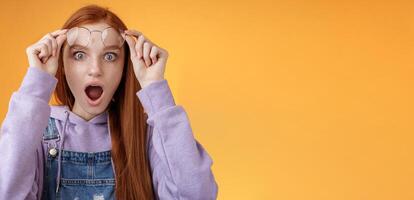 Omg no freakin way. Shocked emotional redhead girlfriend take off glasses speechless drop jaw gasping stunned wide eyes camera stare amazed found out shook secret standing orange background photo