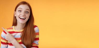 Amused carefree thrilled emotional redhead female fan adore talking favorite movie pointing upper left corner fascinated smiling broadly happy delighted attend incredible party, orange background photo