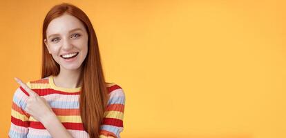 Friendly outgoing good-looking ginger girl university student discussing lecture classmate smiling laughing pointing upper left corner questioned curious know details standing orange background photo