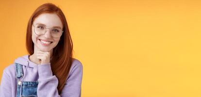 Creative outgoing young charismatic redhead female coworker discuss casual staff smiling laughing happily have pleasant conversation look camera amused tender touch chin, orange background photo