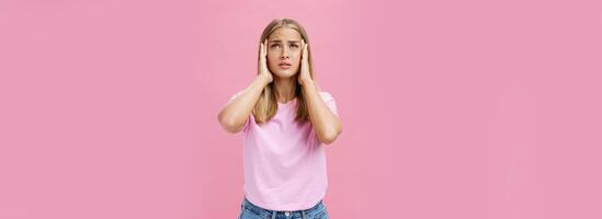 Woman trying recall important number touching temples with hands looking up concerned and focused having trouble to remember information standing intense against pink background photo