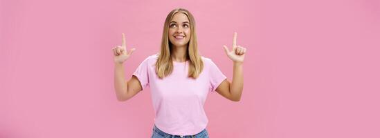 Girl daydreaming pointing and looking with upbeat and admiring expression up smiling cheerfully enjoying nice sunny weather walking in casual t-shirt and jeans posing against pink background photo