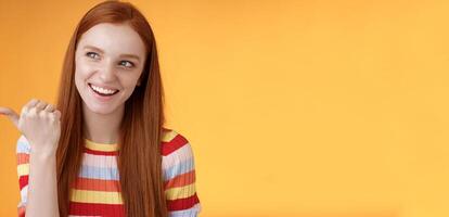 Amused outgoing redhead stylish female student discuss girly things smiling cheeky pointing handsome guy smirking devious pointing thumb looking intrigued curiously staring orange background photo