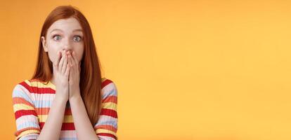 Shocked speechless impressed sensitive redhead european girl reacting stunning rumor gossiping find out secret gasping cover mouth palm stare camera astonished surprised, orange background photo