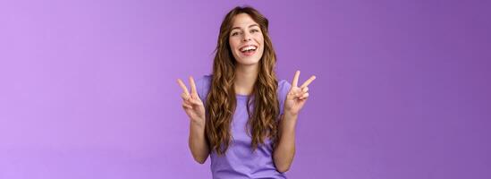 Happy cheerful attractive female express positive upbeat attitude show peace victory signs smiling broadly toothy adorable grin having fun enjoy summer holidays posing photograph purple wall photo