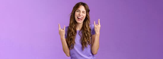 Daring sassy funny attractive woman having fun enjoy awesome party arrange music concert gathering show rock-n-roll heavy metal sign joyful stick tongue wink cheeky purple background photo