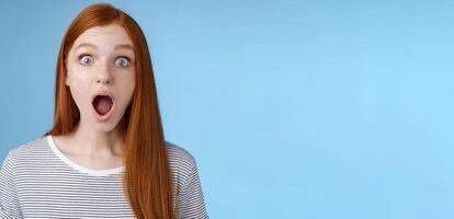 Wow so cool. Impressed speechless amused attractive redhead girl blue eyes freckles open mouth wide omg drop jaw astonished express surprise amazement, standing blue background photo