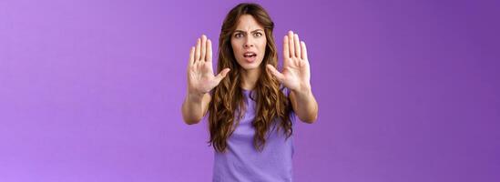 You need stop hold it. Serious-looking intense displeased woman pull hands prohibition taboo sign frowning demand enough shooting me bad mood restict doing mistake purple background photo