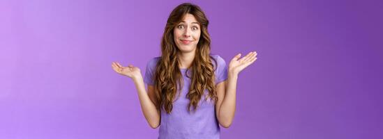 Girl not giving any care. Carefree unbothered cute caucasian curly-haired woman shrugging hands spread sideways smirking uninterseted nothing to say shake head questioned clueless purple background photo