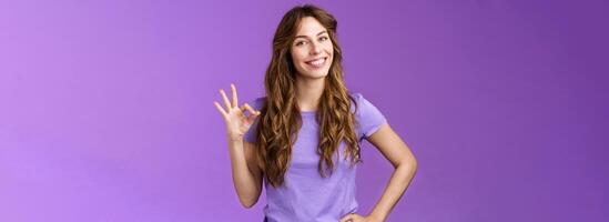 Confident professional girl not scared difficult task assure everything okay smiling broadly self-assured pose hold hand hip show ok ring sign grinning accepting agree good terms purple background photo