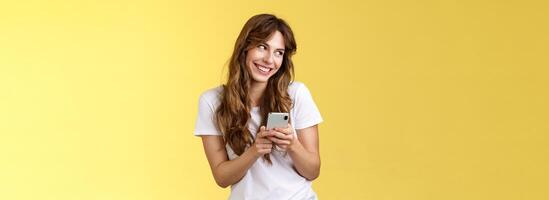 Lovely silly cute flirty girl texting receive romantic lovely gesture look away blushing modest smiling broadly reading bold passionate message stand yellow background joyfully send boyfriend photo