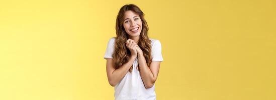 Tender lovely cute curly-haired girlfriend sighing happily clasp hands togehter appreciate touching perfect gift tilt head smiling broadly grateful thanking effort stand pleased yellow background photo