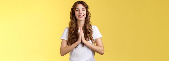 Cheerful confident outgoing young polite girl say namaste greeting asian guests smiling gladly thanking for visit hold hands pray supplication gesture asking favour begging stand yellow background photo