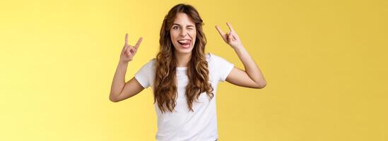 Awesome party having fun. Daring attractive carefree girl enjoy excellent event show rock-n-roll heavy metal gesture mimicking funny expressions wink stick tongue stand yellow background amused photo