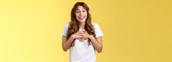 sorprendido tocado agradecido encantador caucásico pelo rizado hembra apreciar esfuerzo agradeciendo increíble regalo prensa manos corazón movido encantador bonito presente sonriente en general agradecido amarillo antecedentes foto