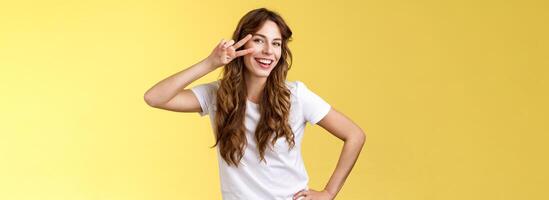 Girl having fun feel happy enthusiastic enjoy perfect summer day share positivity upbeat mood show peace victory sign near cheek tilt head smiling silly carefree stand yellow background photo