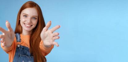 Come into arms. Charming sincere happy kind redhead girl baby sitting stretch hands camera wanna hold catch smiling friendly asking pass object, standing blue background reach friend give cuddles photo