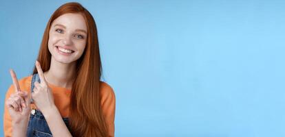 Happy tender redhead girl sincerely smiling white teeth helpful look camera excited give hand pointing upper left corner introduce sale offer recommend try promo standing blue background photo