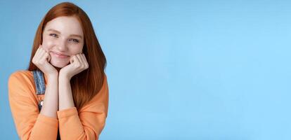 Tenderness, wellbeing, beauty conept. Attractive young ginger girl pure skin blue eyes lean palms silly smiling camera look amused enthusiastic listen interesting stories gladly, blue background photo