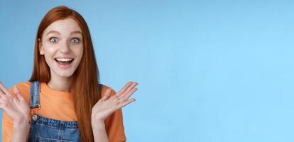 Surprised delighted happy friendly-looking amused redhead female friend learn incredible good news congratulating girlfriend fascinated wide eyes camera joyfully clap hands amazed, blue background photo