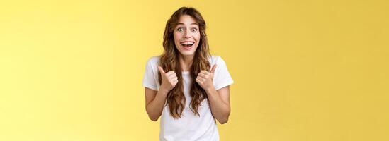 Lively excited happy cute european girl supportive give positive reply think event awesome smiling broadly show thumbs-up approval, accept great choice stand yellow background thrilled photo