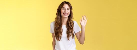 saliente cómodo relajado simpático casual europeo mujer Rizado Corte de pelo ondulación elevado palma decir Hola introducir sí misma volverse nuevo miembro sonriente en general saludo Hola gesto amarillo antecedentes foto