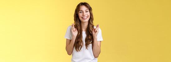 Girl faithfully believe dream come true hopefully awaiting positive results smiling broadly cross fingers good luck implore god good news stand excited optimistic yellow background photo