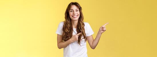 Lively surprised happy cheerful smiling happy girl long curly haircut grinning toothy white perfect grin point index finger left sideways discuss new furniture move in appartment show friends photo