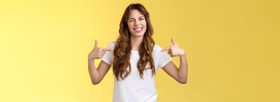 You would not regret this. Sassy good-looking outgoing daring young woman pointing center copy space indicating herself winking joyfully show perfect candidature stand yellow background photo