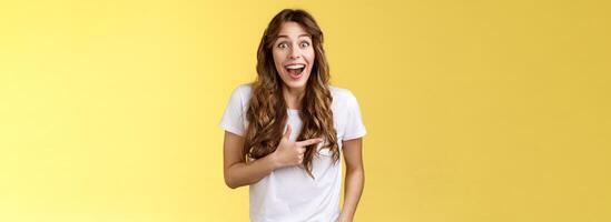 Joyful charismatic woman having fun chatting friend have funny amusing conversation discuss comedy movie pointing left fascinated impressed open mouth smiling broadly laughing yellow background photo