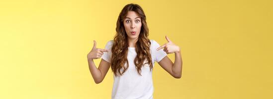 Wow just look. Impressed surprised cute wondered european girl pointing fingers center copy space white t-shirt folding lips amused astonished awesome promo great chance gaze you camera photo