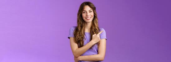 Cheerful smart confident assertive curly-haired caucasian female share link pointing index fingers upper left corner smiling broadly give advice what place visit stand purple background photo
