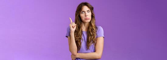 Strict funny curly-haired girl pulling disappointed angry face popping eyes stare camera shaking index finger disapproval scold bad behaviour stand serious bossy purple background photo