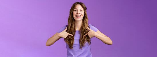 Boastful good-looking curly european female pointing herself proud who she is grinning delighted coming out pride month smiling broadly indicating center chest bragging purple background photo